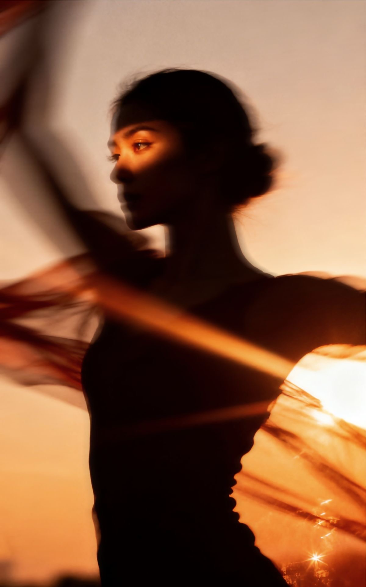 Mulher em movimento entre lençóis iluminados por luz dourada